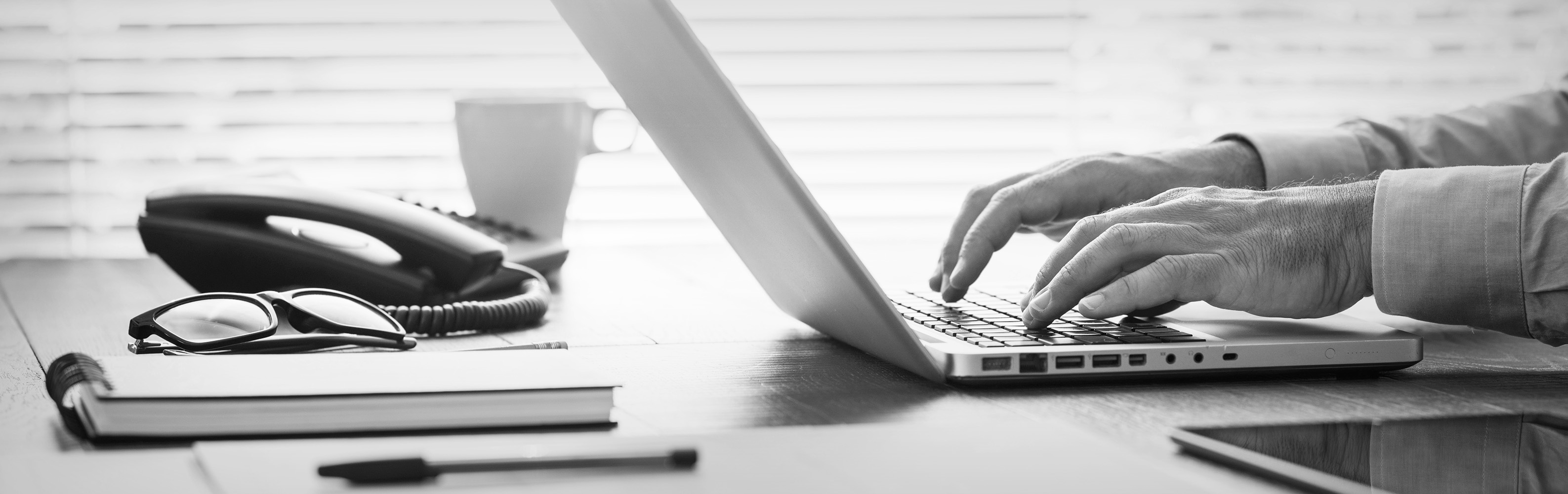 Schwarz-weißes Bild mit Laptop, Tasse und Telefon auf dem Tisch Schwarz-weißes Bild mit Laptop, Tasse und Telefon auf dem Tisch