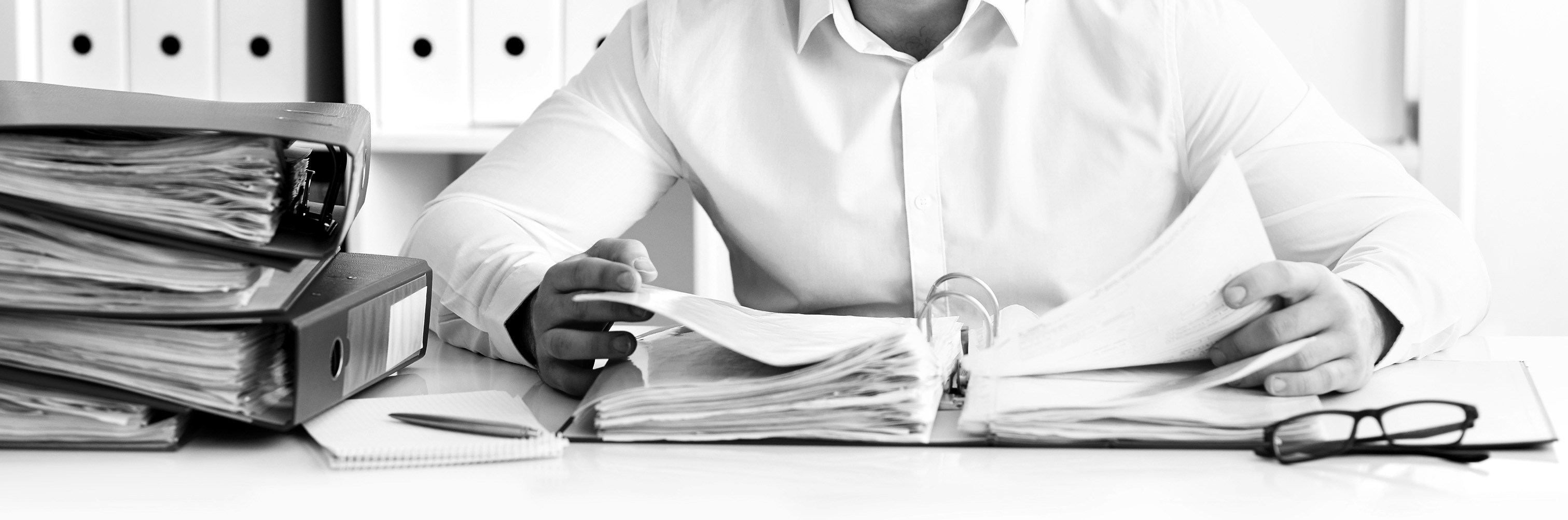 Person sitzt am Schreibtisch und blättert im Ordner Person sitzt am Schreibtisch und blättert im Ordner